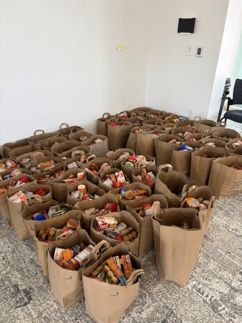 Dozens of paper grocery bags filled with donated food arranged on the floor.