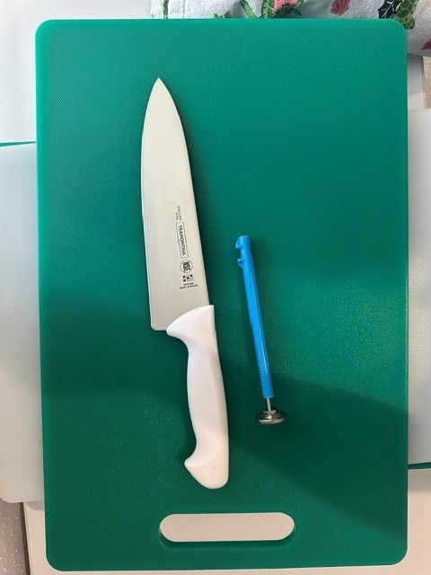 A chef's knife and a vegetable peeler resting on a green cutting board.